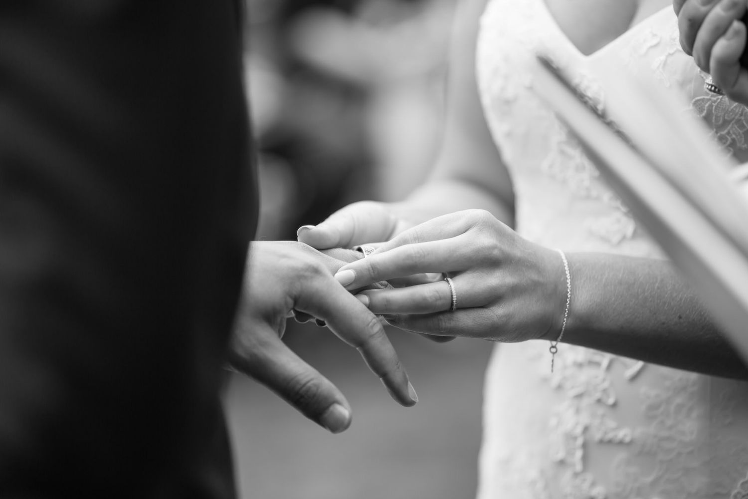 Black and white close-up of hands exchanging wedding rings during a marriage ceremony.