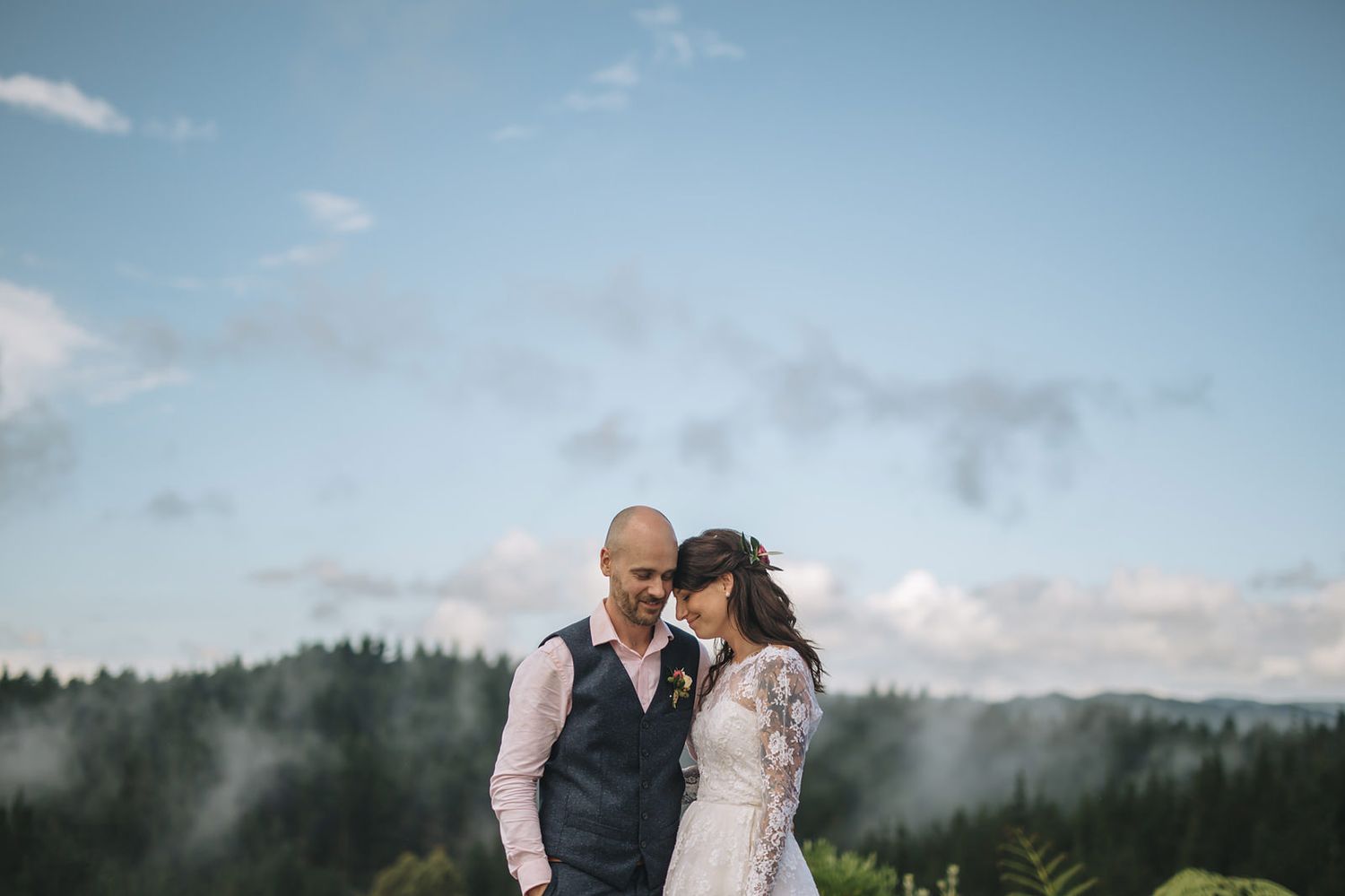 A couple embraces outdoors with misty mountains and forest backdrop during an intimate wedding photoshoot.