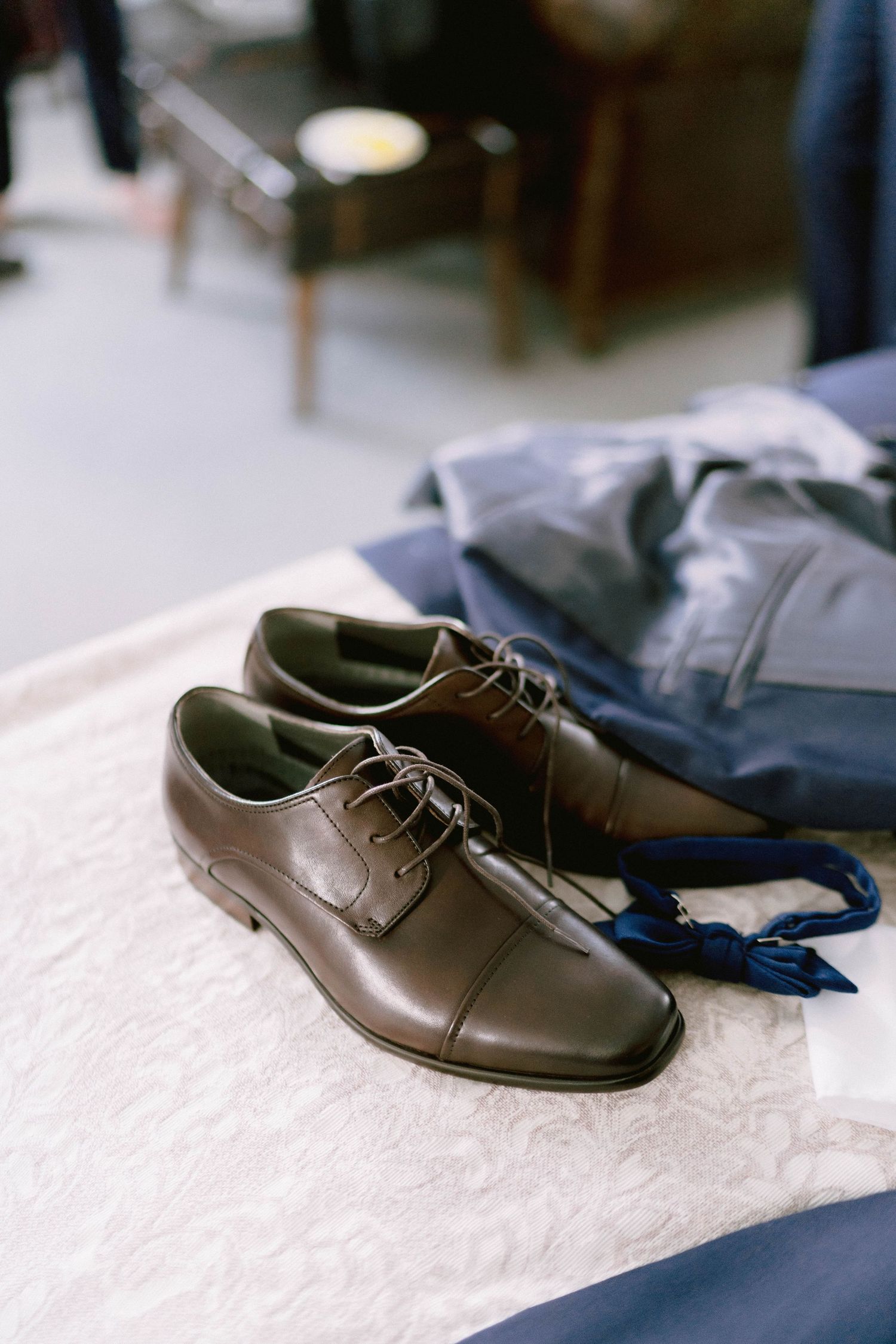 Brown leather dress shoe displayed on white surface with navy fabric in background.