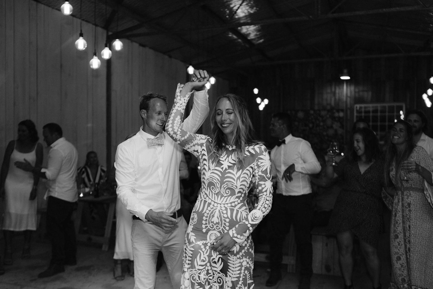 People enjoying themselves dancing at what appears to be a wedding reception or party with string lights overhead.