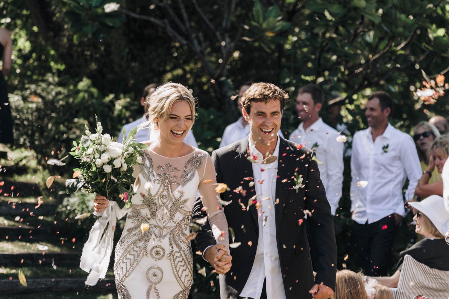 Newlyweds celebrate with confetti during outdoor garden wedding ceremony in elegant attire.