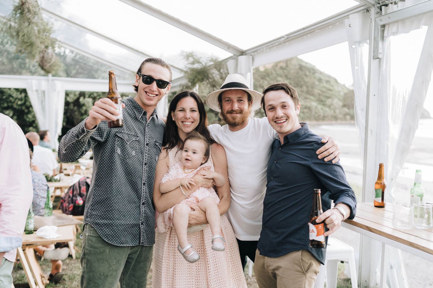 A group of friends celebrating together under a white tent at an outdoor party.