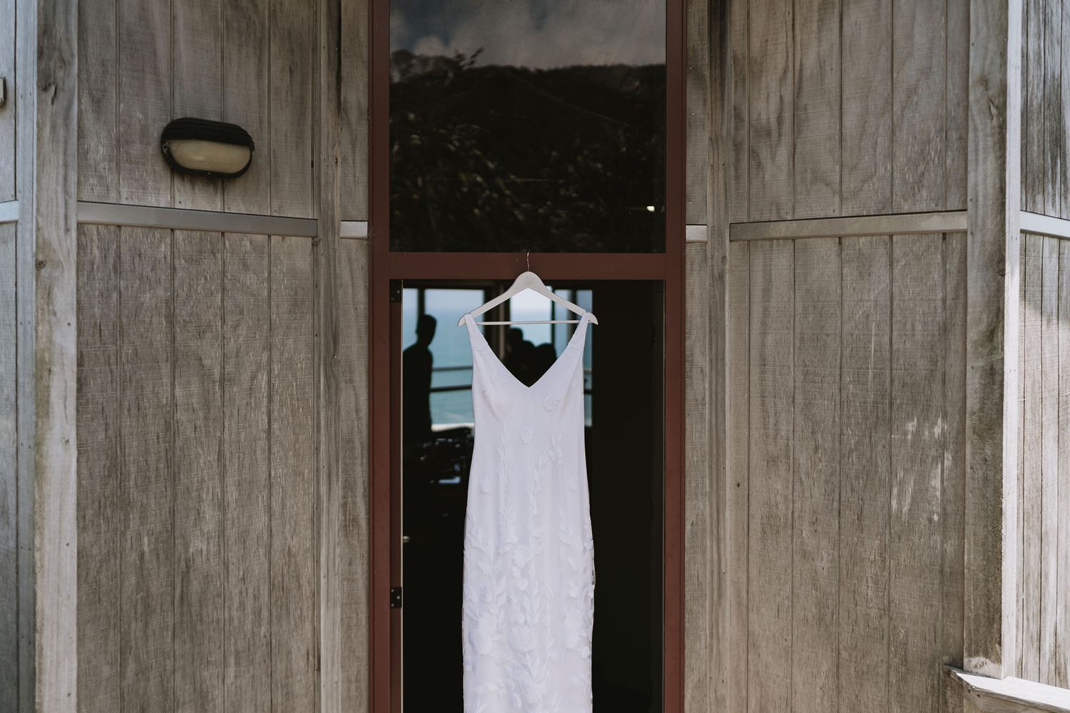 A white wedding dress hangs in a doorway of a rustic wooden building.
