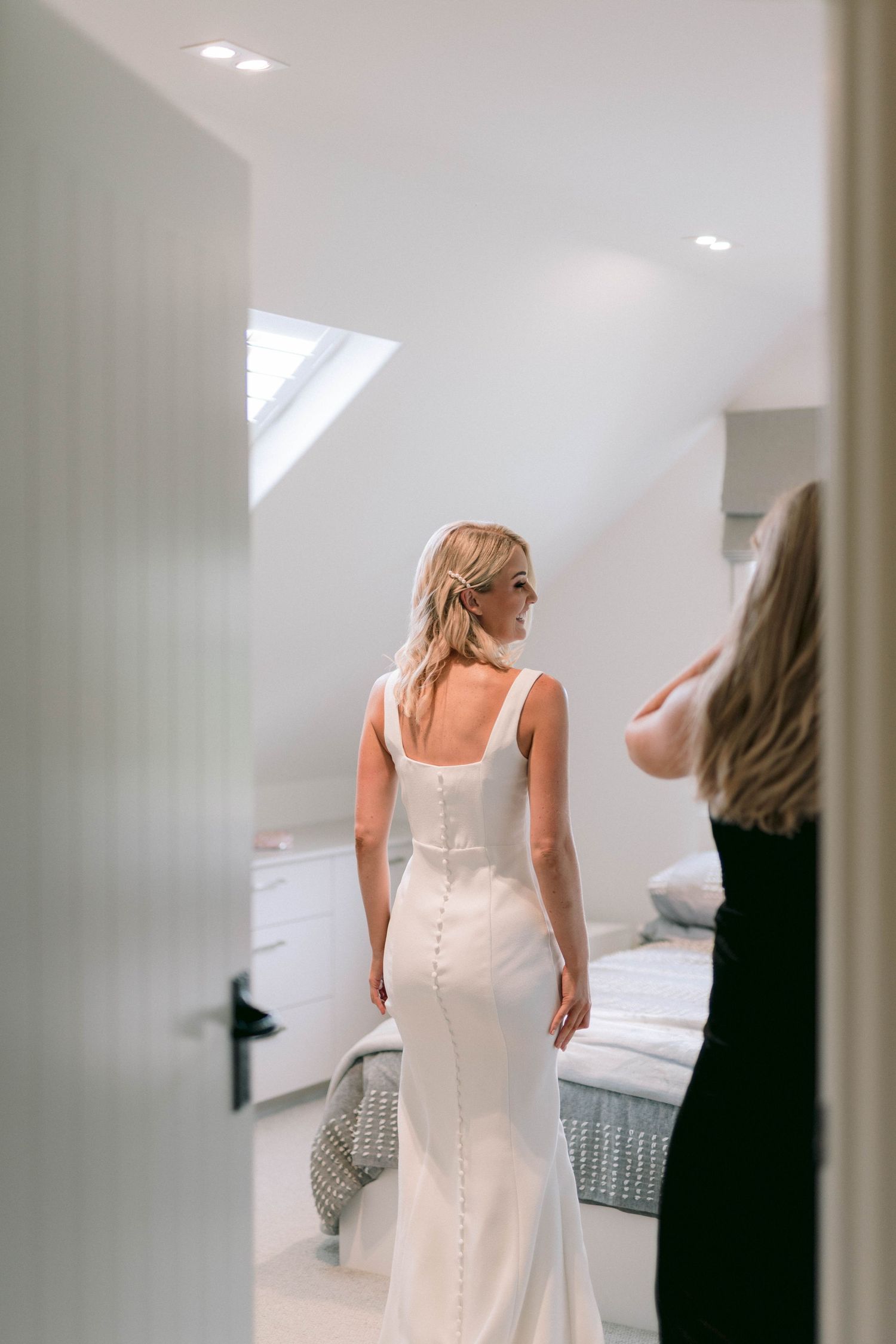 A fitted white wedding dress with elegant button detail down the back in a bright dressing room.