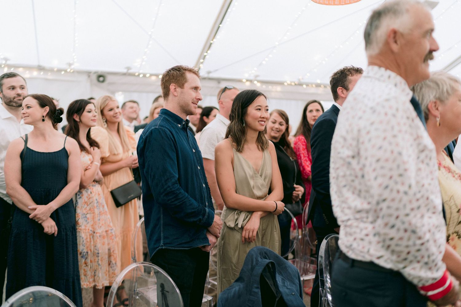 Wedding guests dance and socialize at an outdoor tented reception with festive lighting.