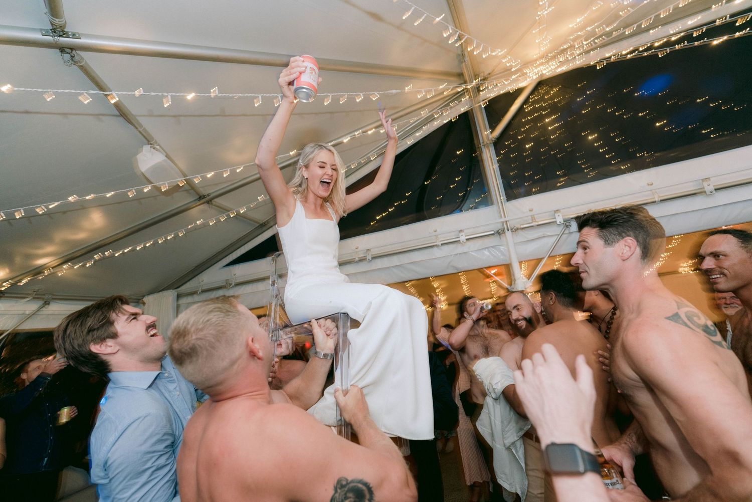 A wedding celebration with guests lifting the bride during a reception party.