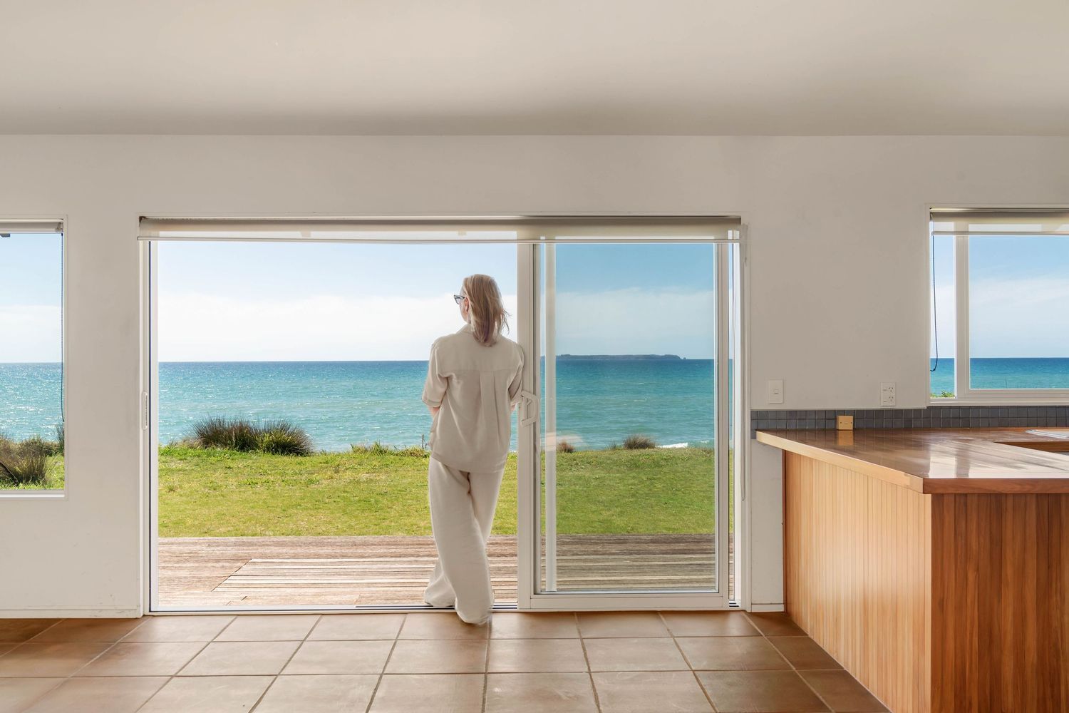 Modern oceanfront room with tiled floor features large glass doors opening to stunning turquoise water views.