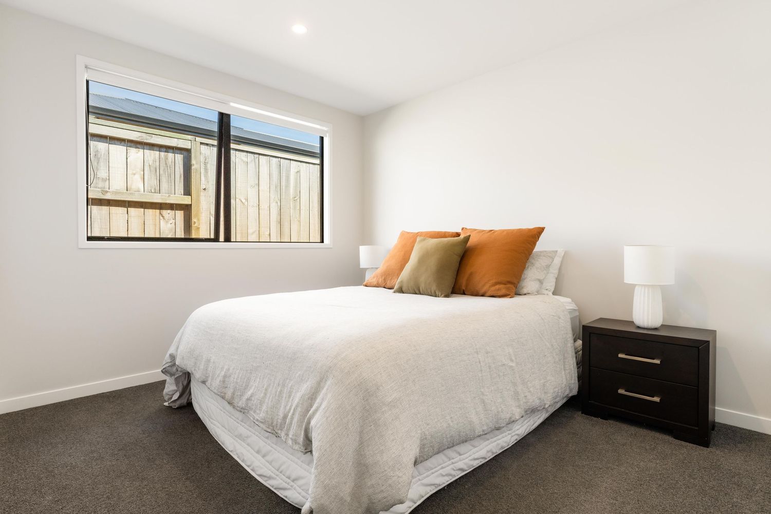Bright modern bedroom with white walls, gray carpet flooring and natural light streaming through windows.