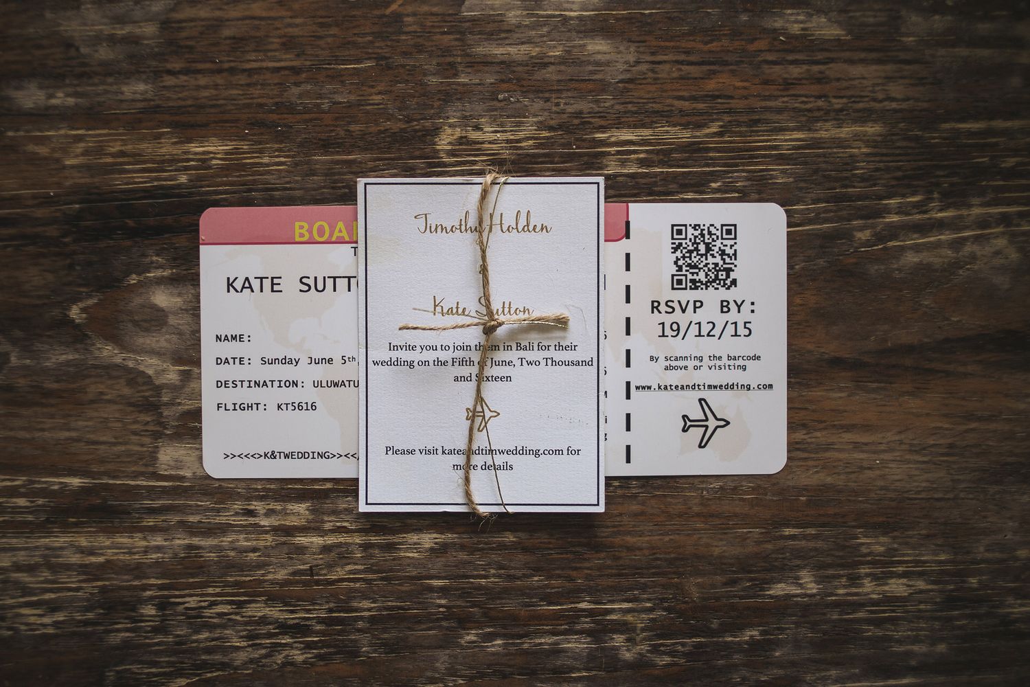 Wedding invitation suite with travel-themed boarding pass design laid on rustic wooden surface.