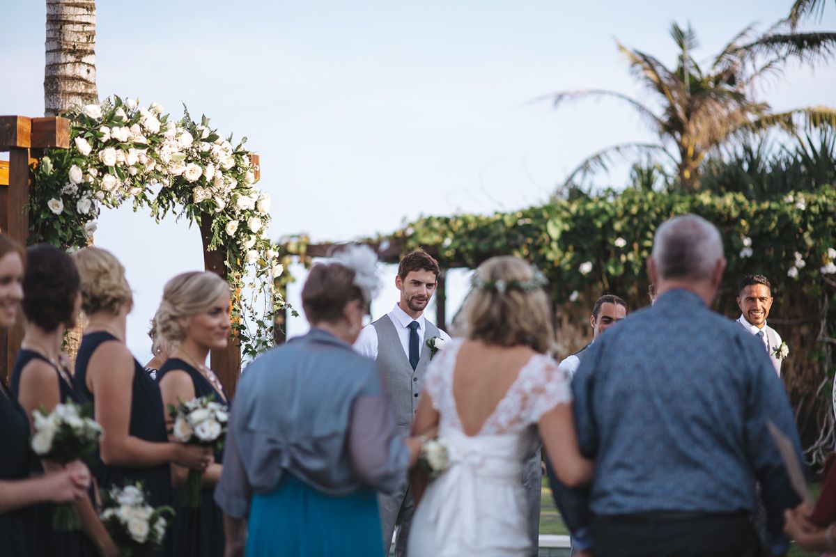 Scenic outdoor wedding ceremony setup with palm trees and ocean view in the background.