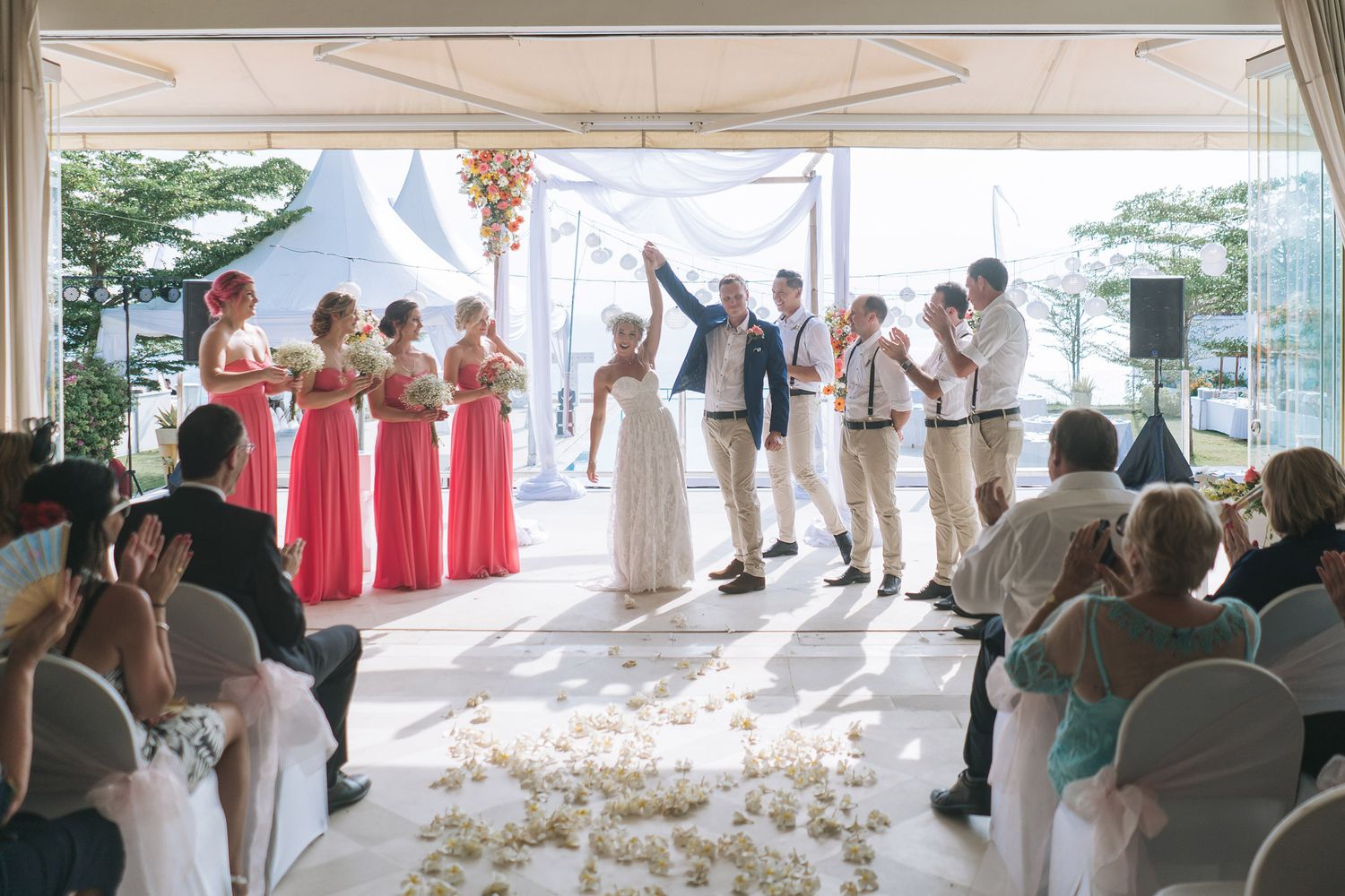 Wedding ceremony under white tent with wedding party and guests celebrating at beachside venue.