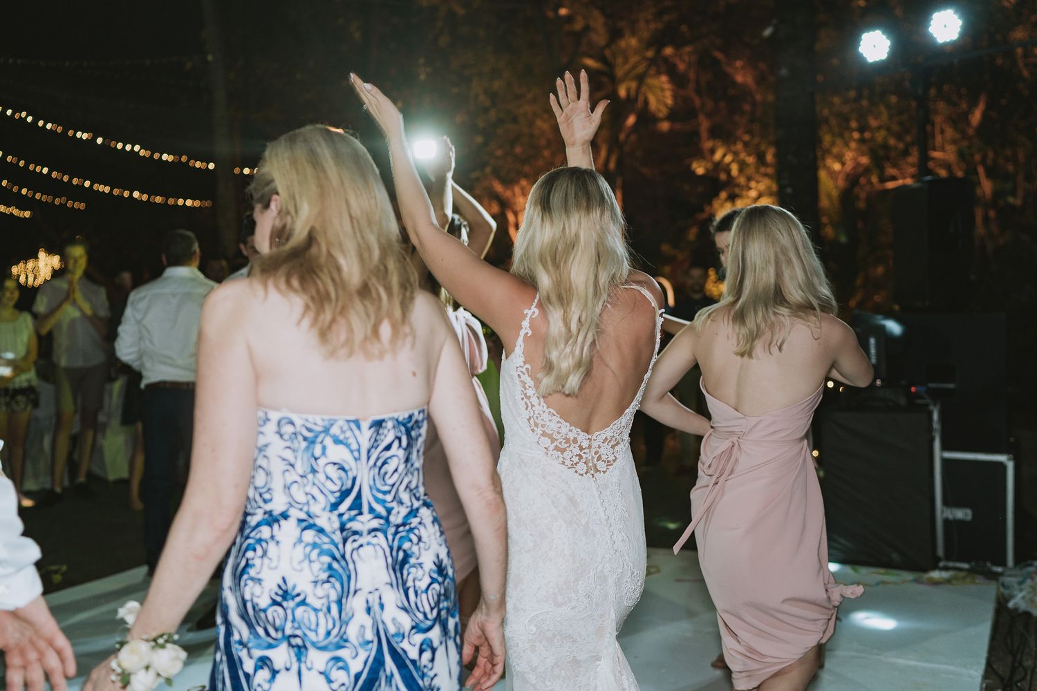 A group of party guests dancing on an outdoor dance floor at night under string lights.