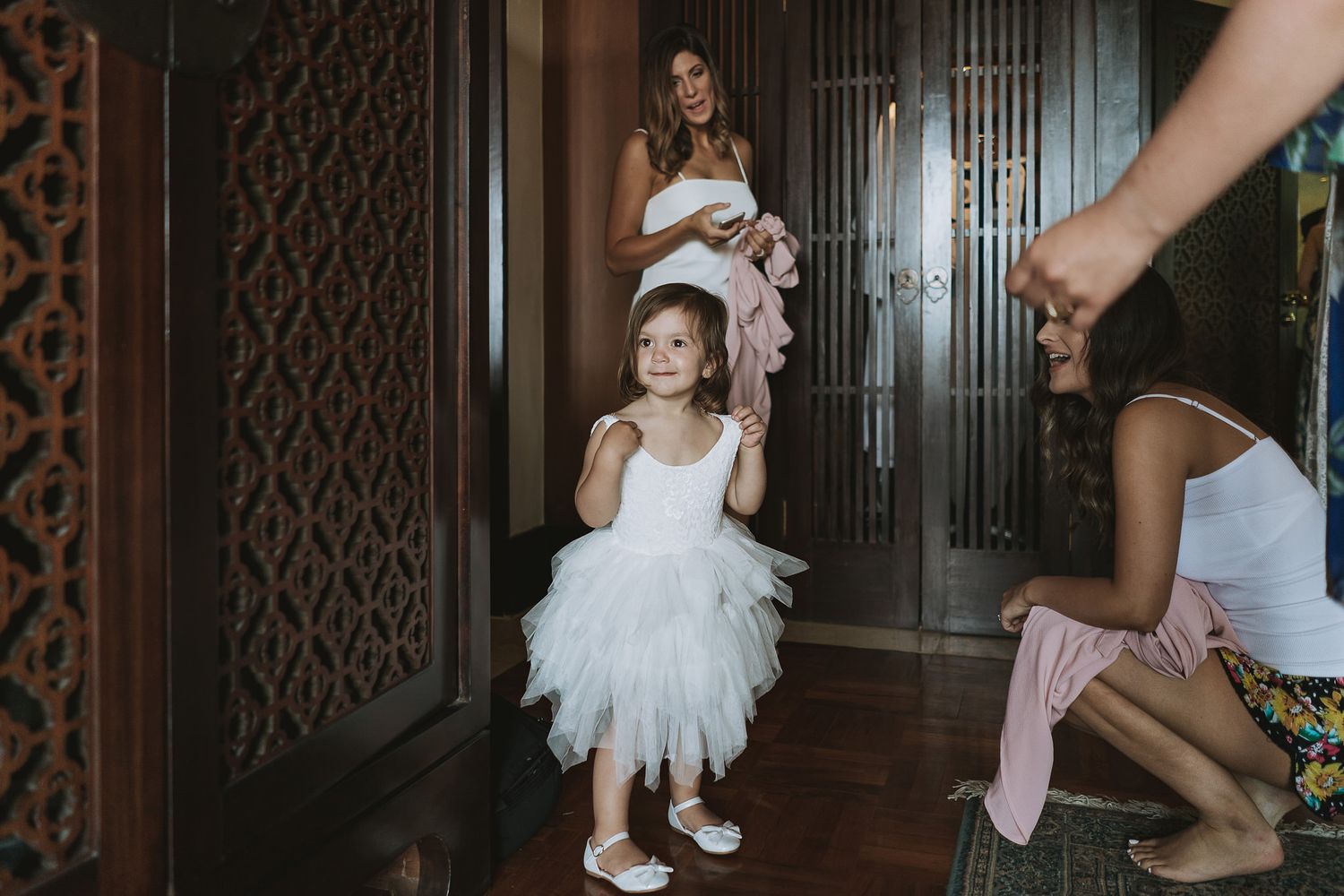 Young child in white tulle dress standing in ornate hallway during wedding preparations.