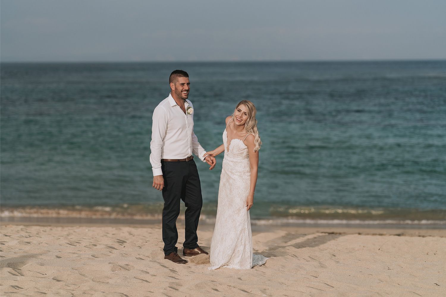 Couple poses on beach with turquoise ocean backdrop in destination wedding photo.