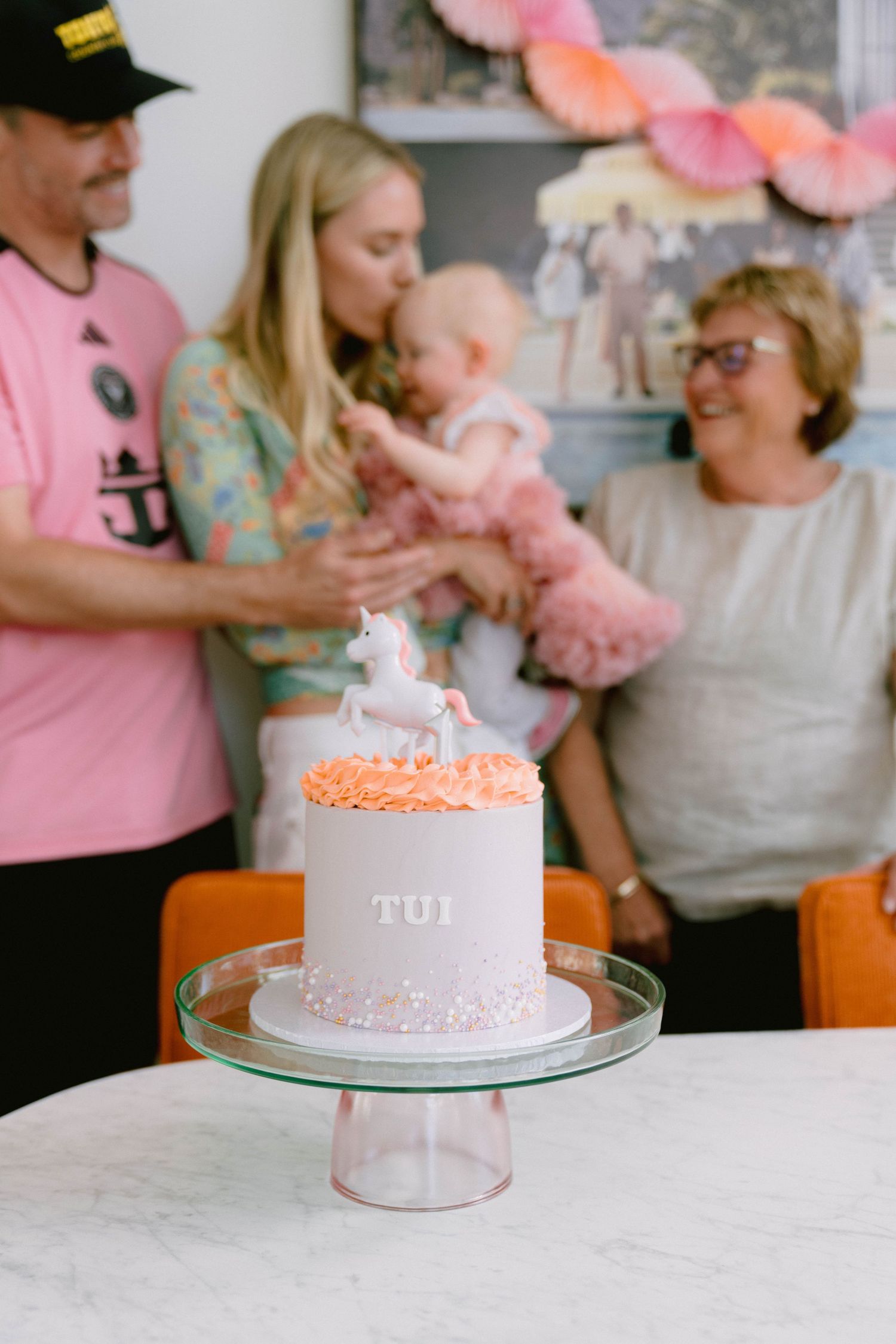 A series of pink themed birthday cake decorations displayed on stands against a marble counter at a celebration.