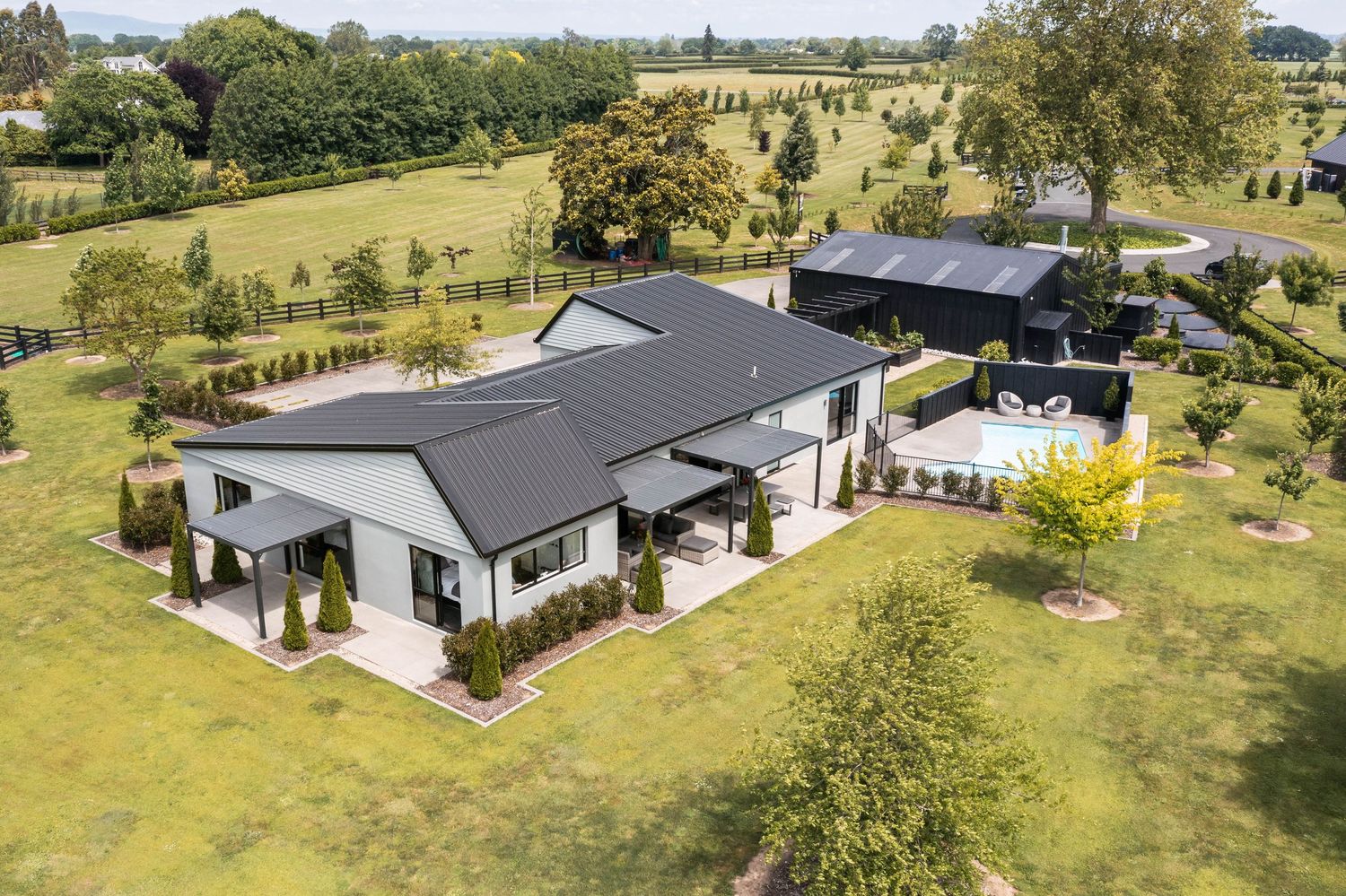 Modern single-story home with dark exterior sits on sprawling rural property with manicured landscaping.