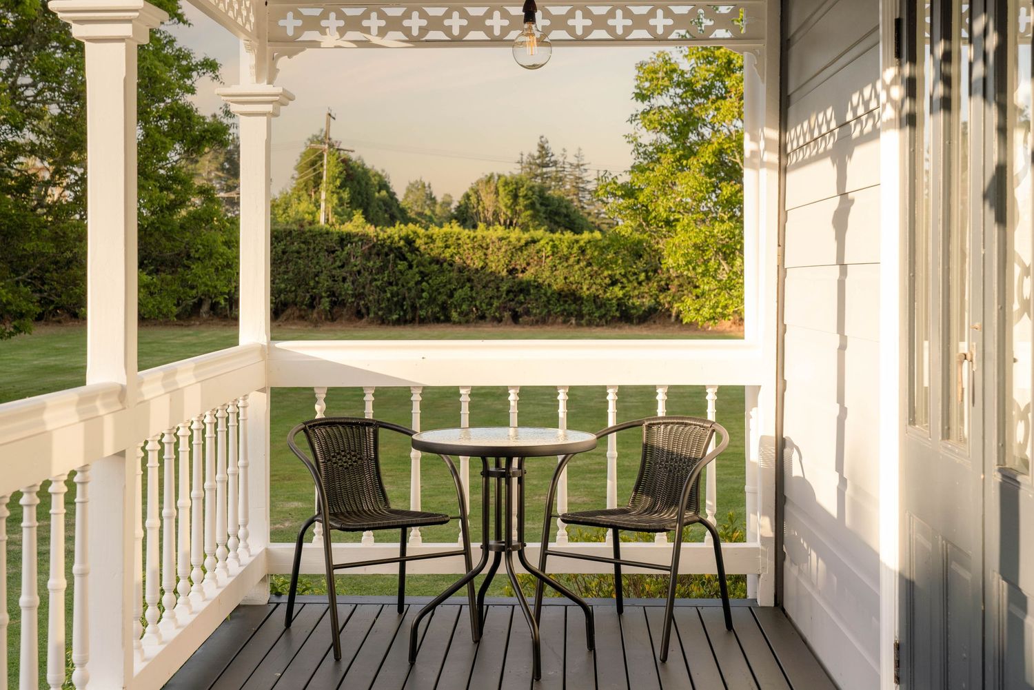 Elegant white wraparound porch with decorative trim and comfortable outdoor seating area in natural light.