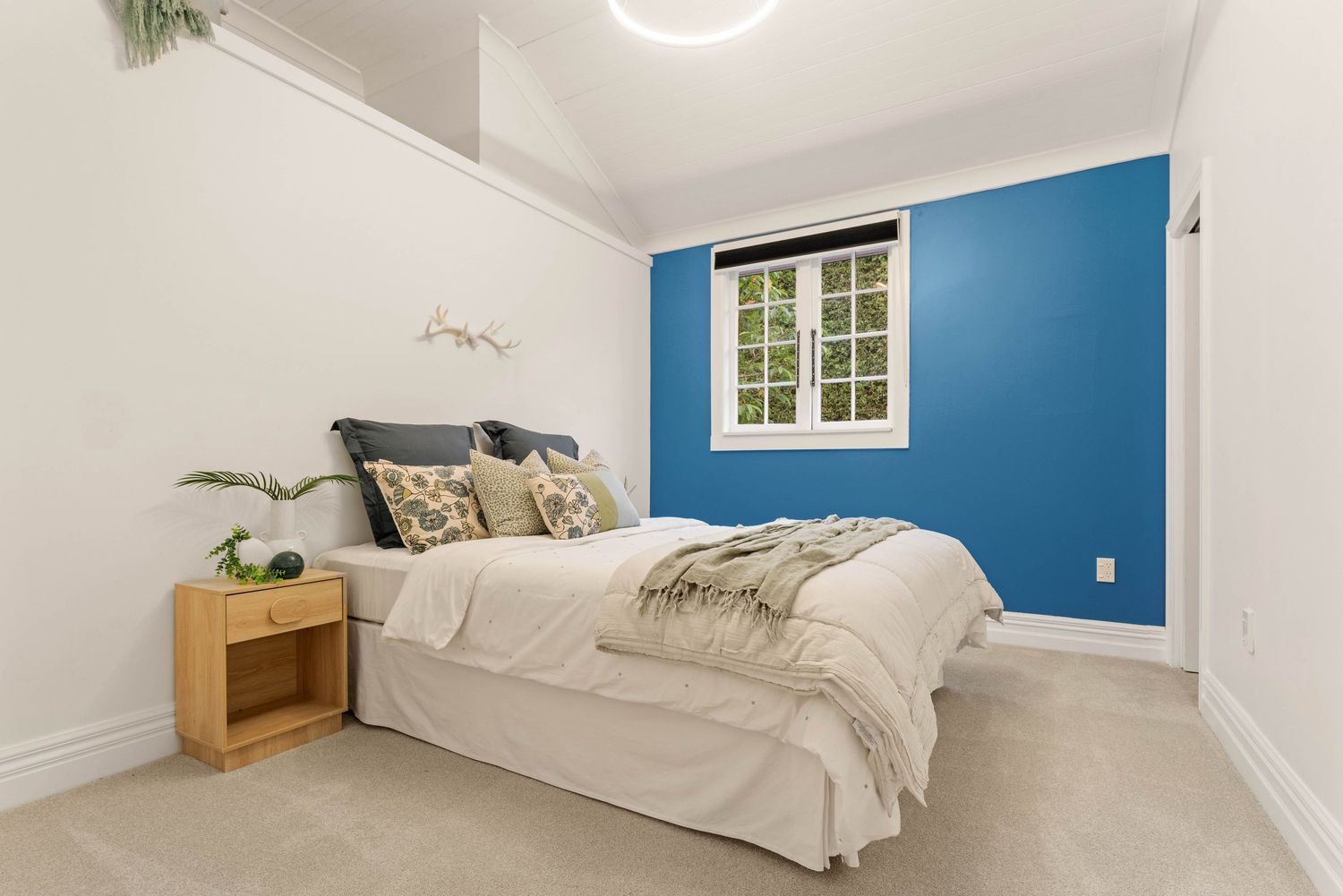 Modern bedroom with bold blue accent wall, white bedding, and wooden nightstand in a minimalist style.