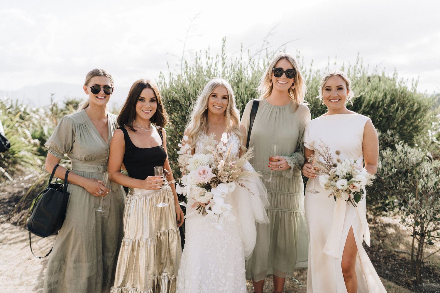 Bridal party in coordinated sage and neutral dresses posing outdoors.