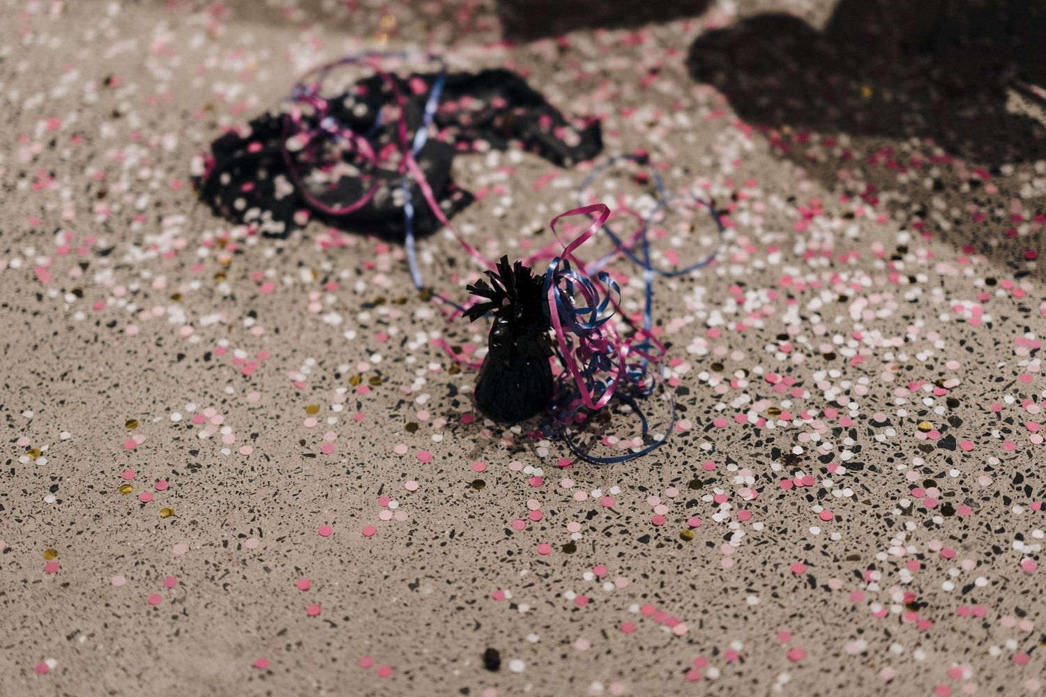 Pink confetti and scattered decorative items lay on concrete ground after a celebration.