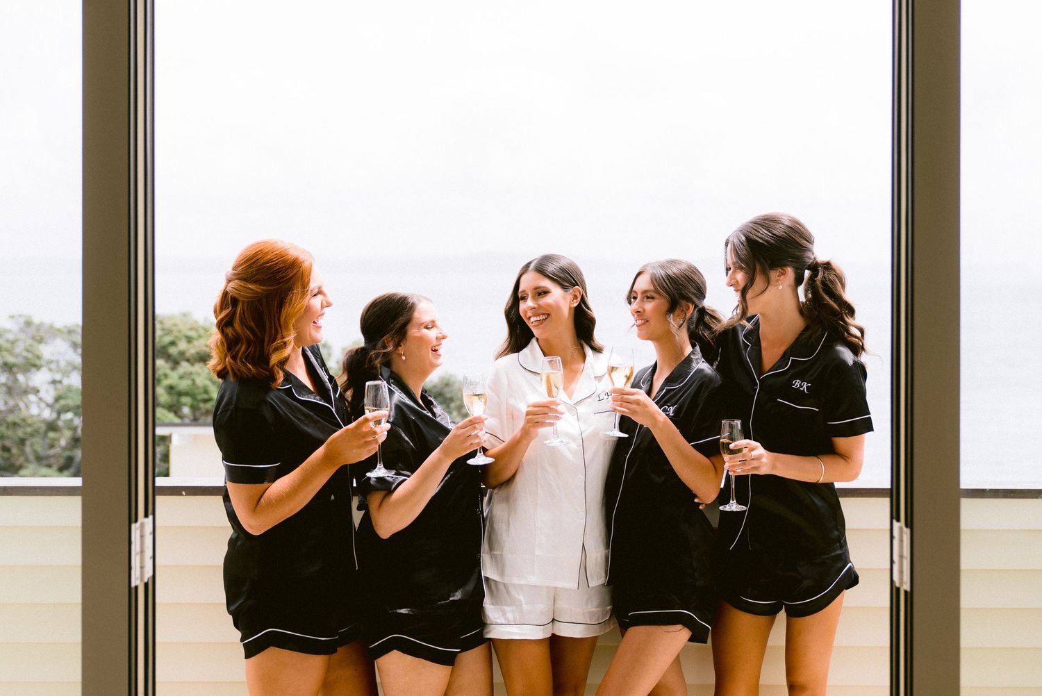 Group celebrating with champagne by large windows in matching black outfits.
