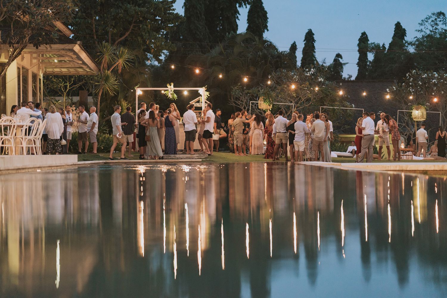 Evening wedding reception by a pool with string lights creating a magical atmosphere.