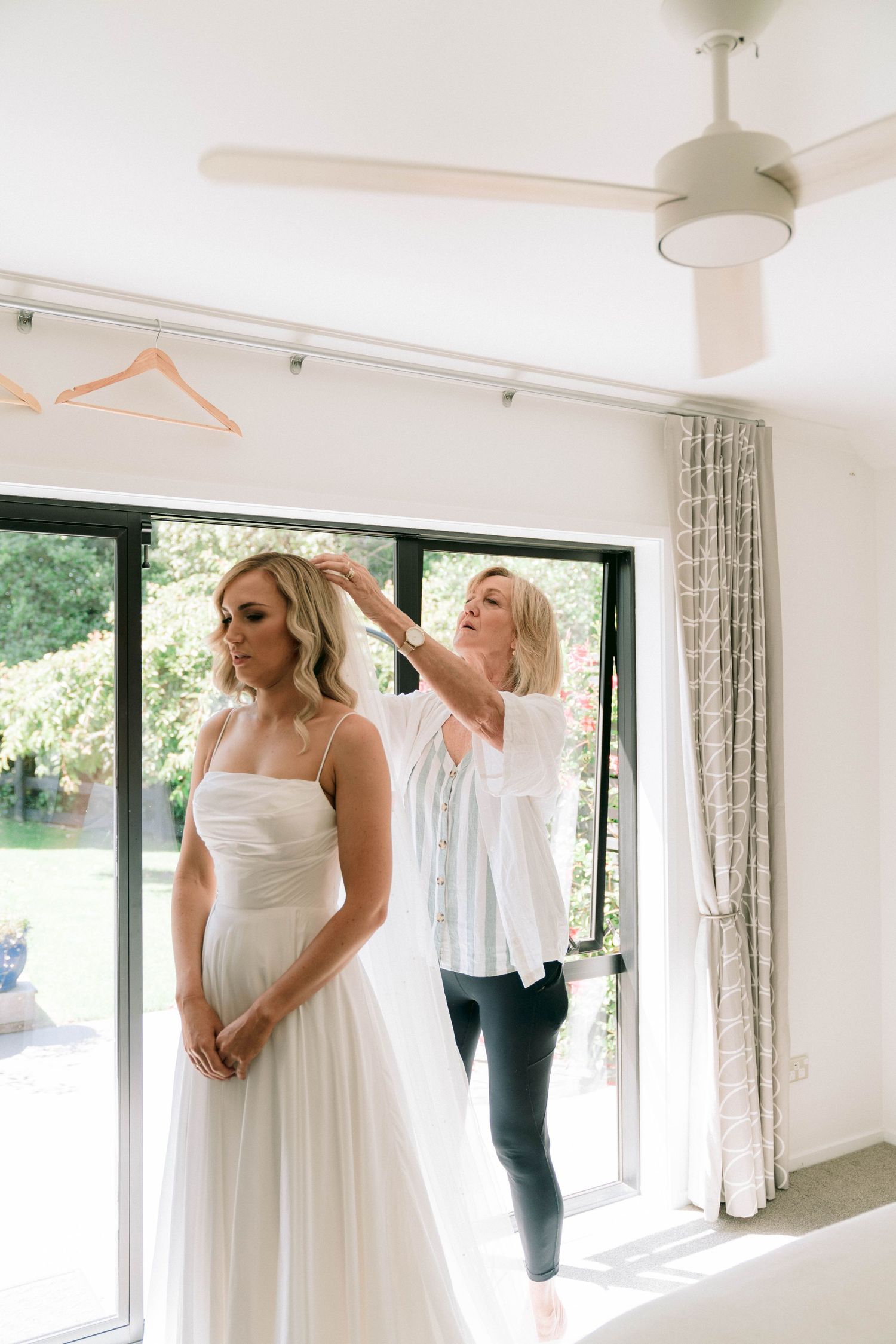 Preparing for a wedding as someone admires a white wedding dress in a bright room with large windows.