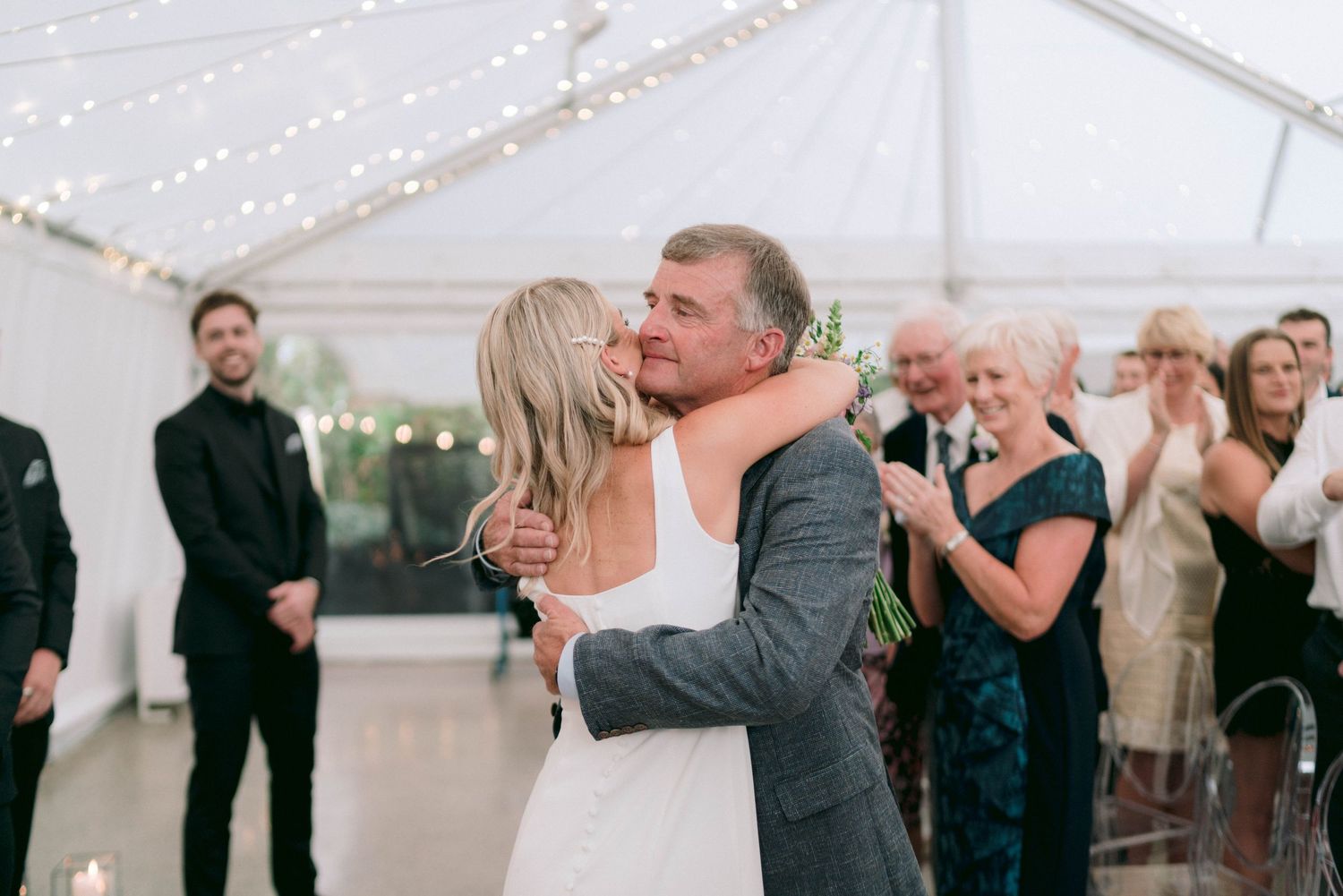 Guests enjoy a lively celebration at a wedding reception inside an elegant white tent venue.