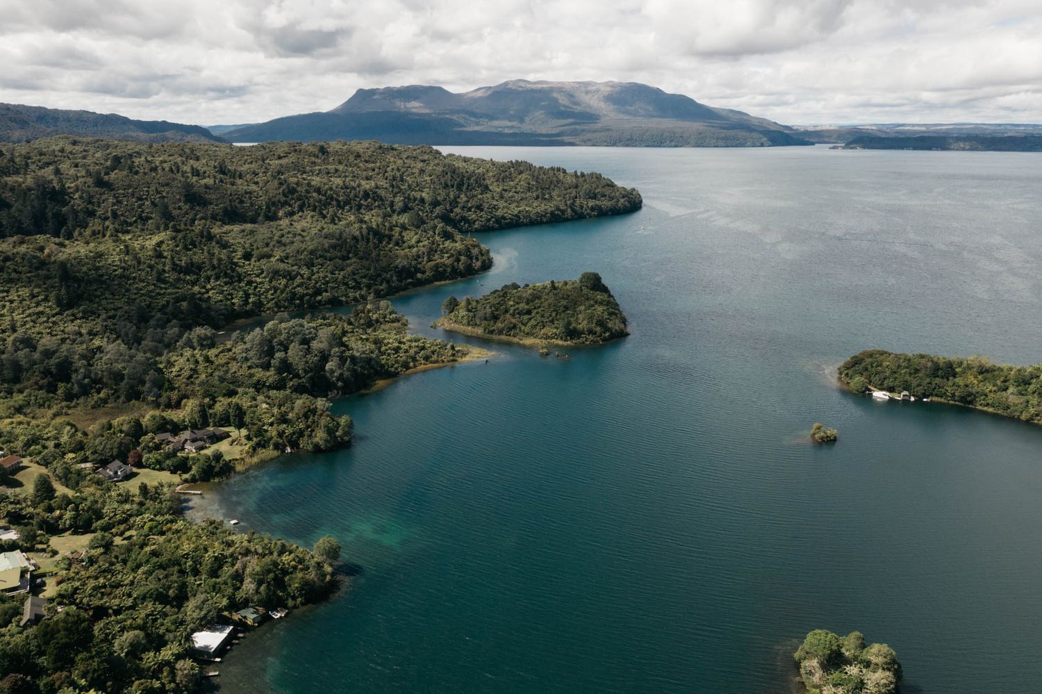 Panoramic aerial view of Lake Taupo in New Zealand showing turquoise waters bordered by lush green hills and distant mountains.
