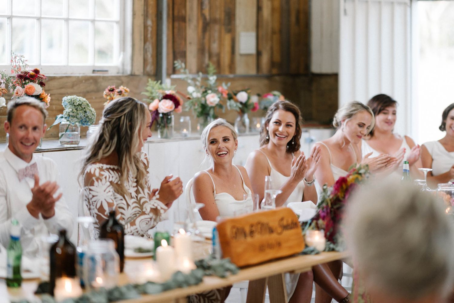 Wedding party gathered at reception table with rustic decor and candlelight in elegant venue.