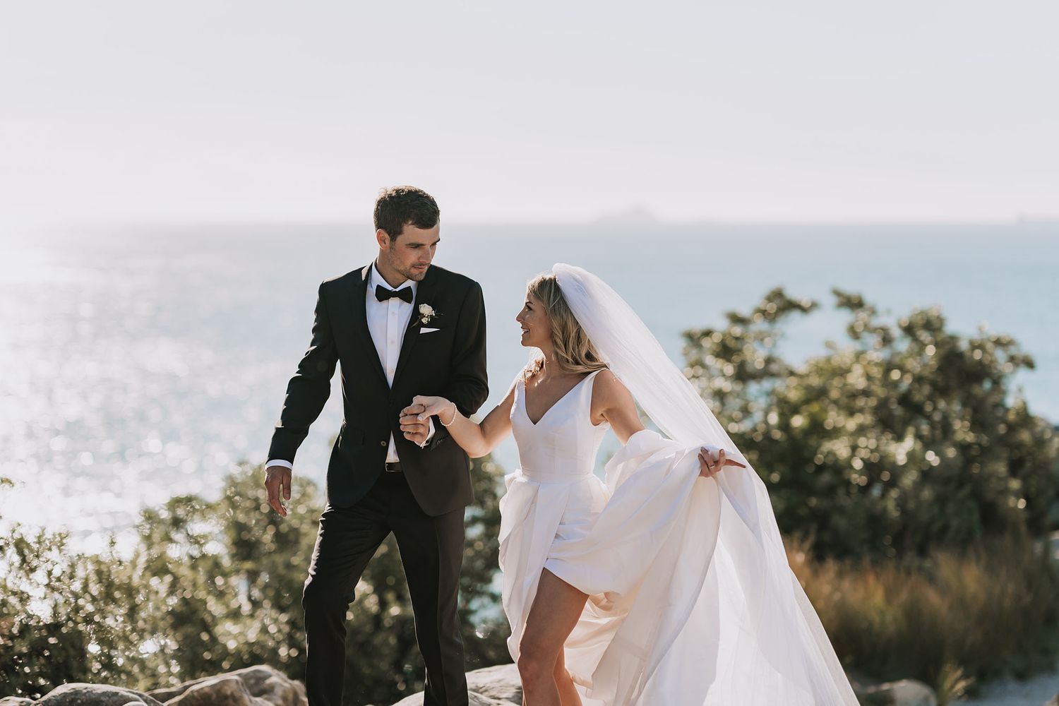 A couple in wedding attire embraces while laughing together in an outdoor setting with soft natural lighting.