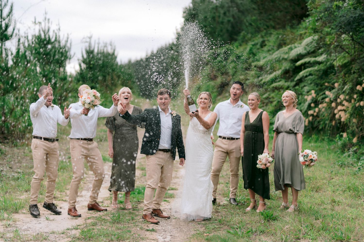 Wedding group celebrates with confetti toss in an outdoor garden setting.