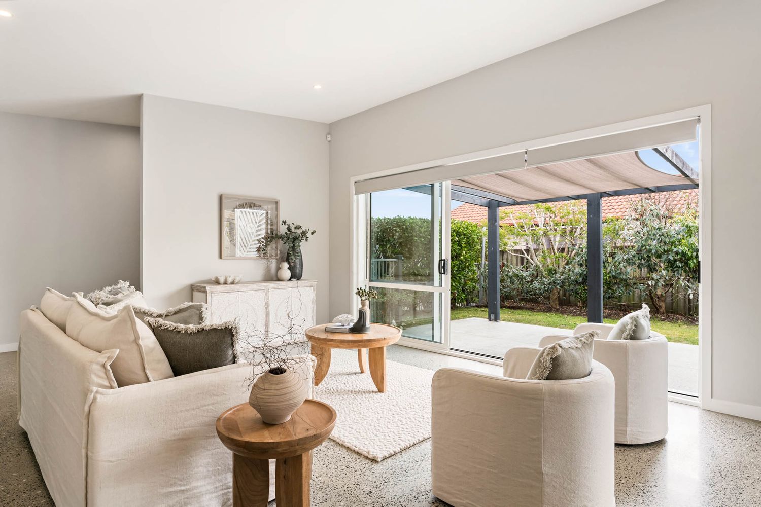 Modern living room with beige furniture and sliding glass doors opening to a covered patio and garden view.