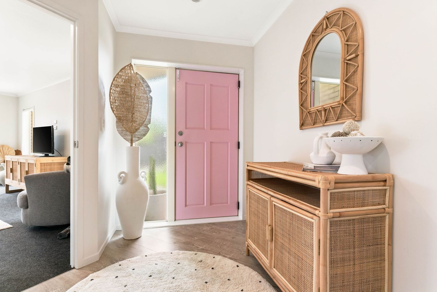 Bright entryway with pink door, rattan console table, and decorative round mirrors in coastal style.