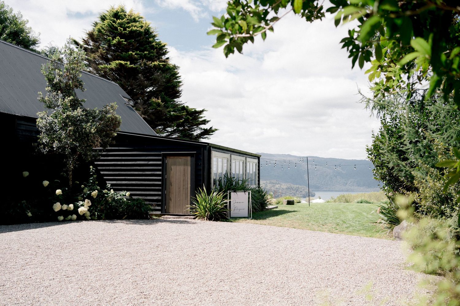 Modern black cabin with gravel driveway overlooking mountain views through lush greenery.
