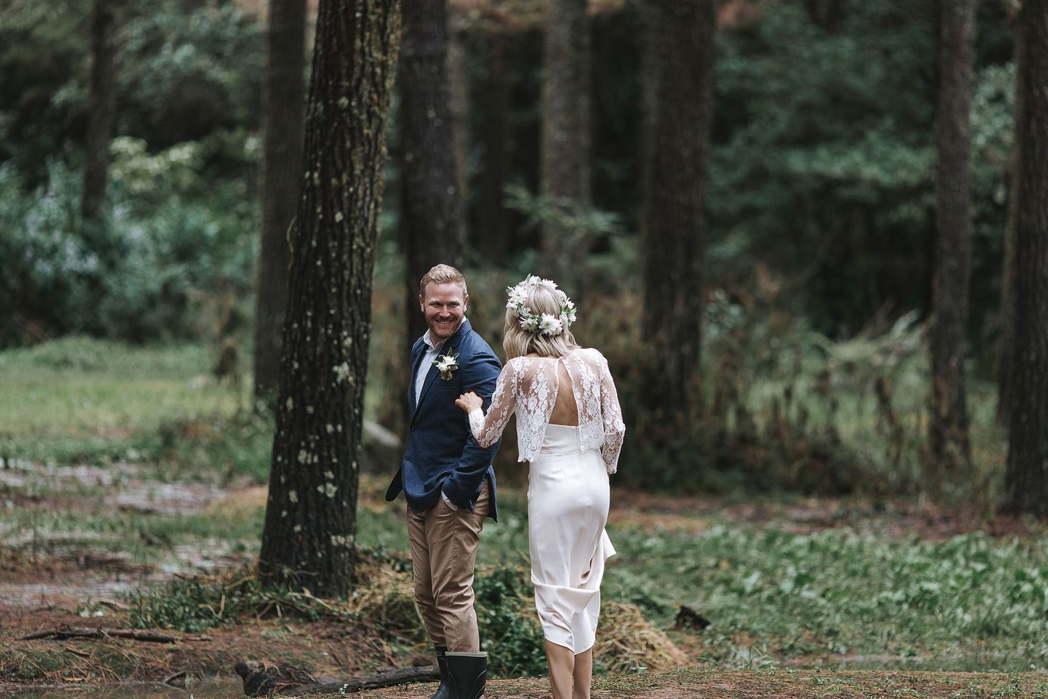 A couple walks through a tall pine forest during a woodland engagement session.