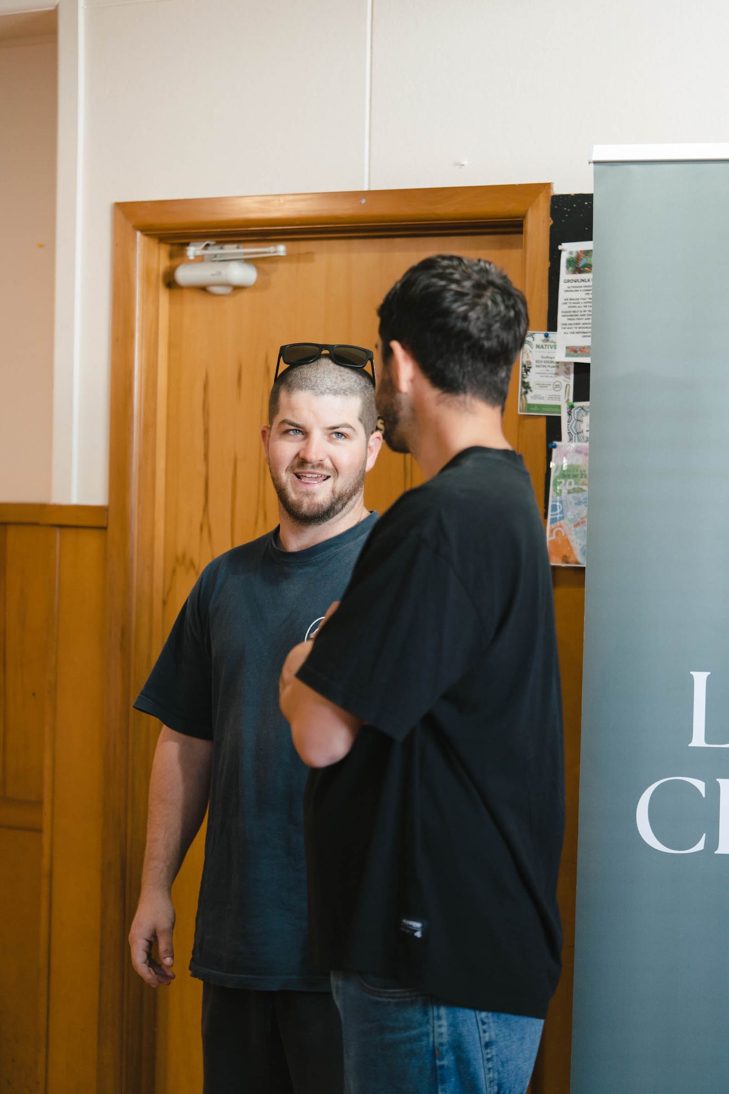 People in black shirts talking in a hallway with wooden panels.