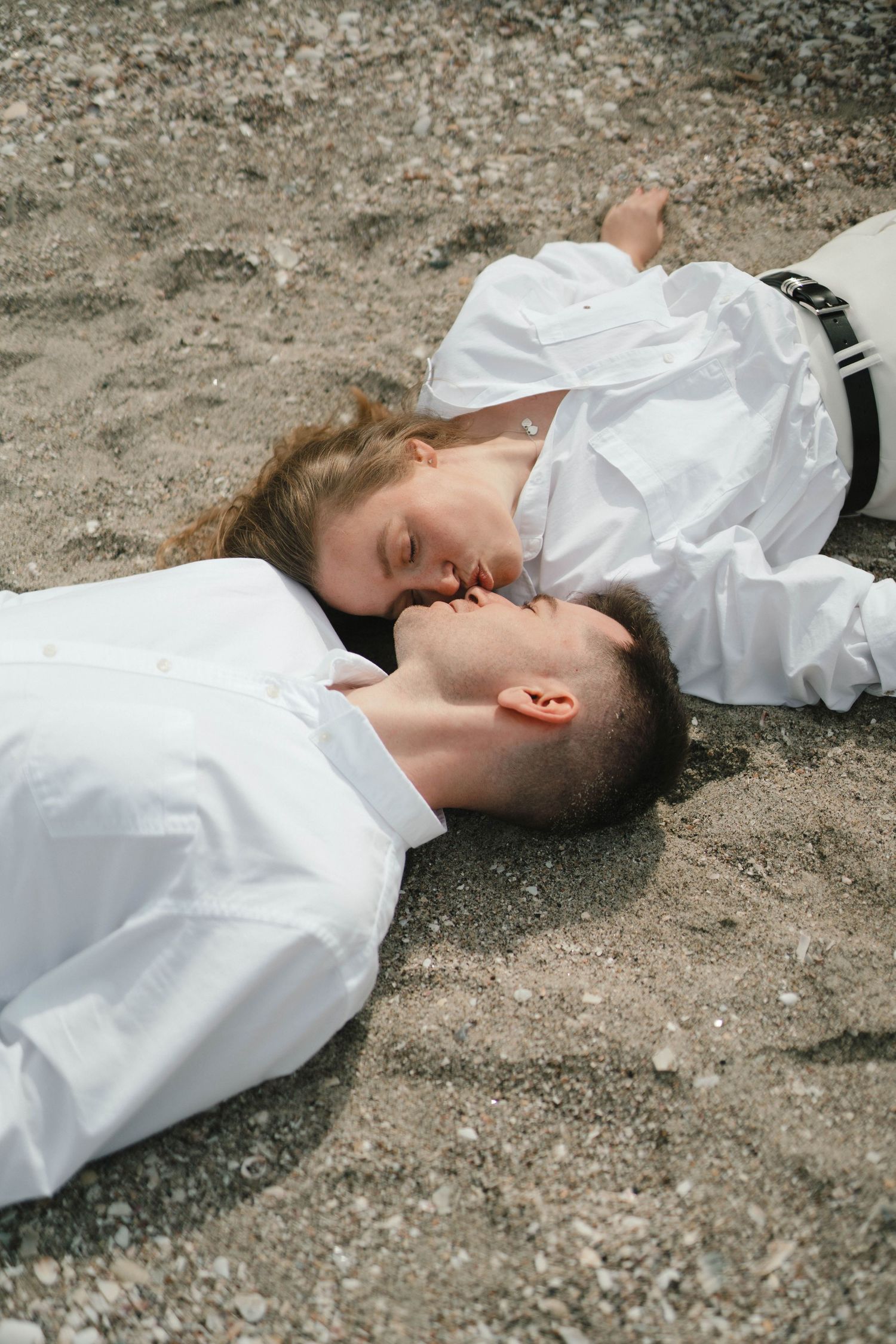 A couple in white clothing lying close together on the ground during an intimate photo session.