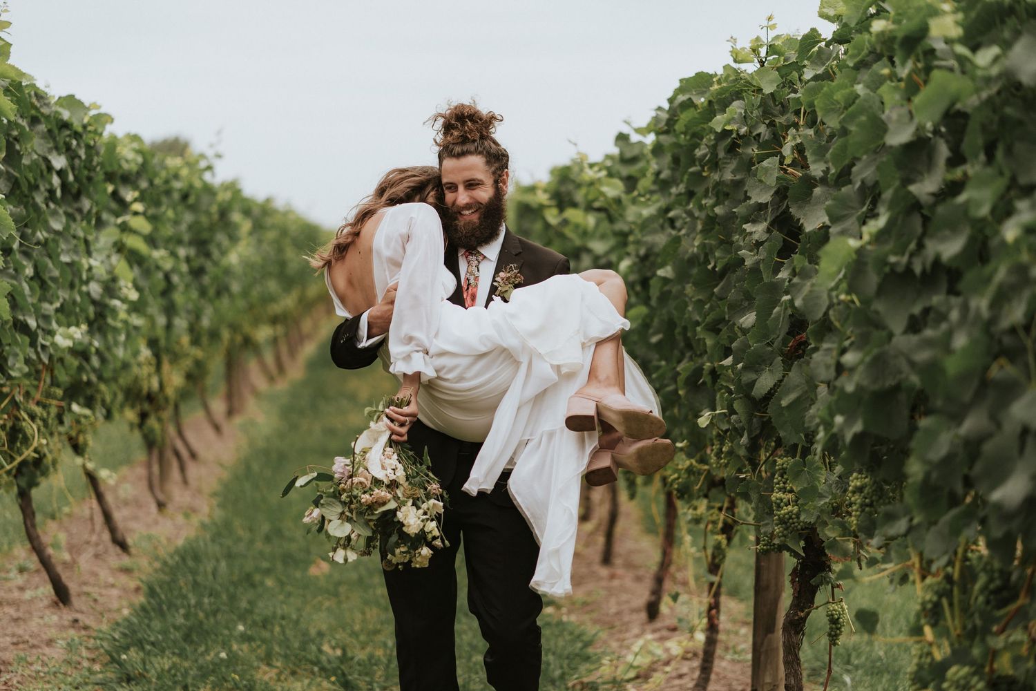 A couple exploring and enjoying a sunny day among lush green grapevines in a picturesque vineyard.