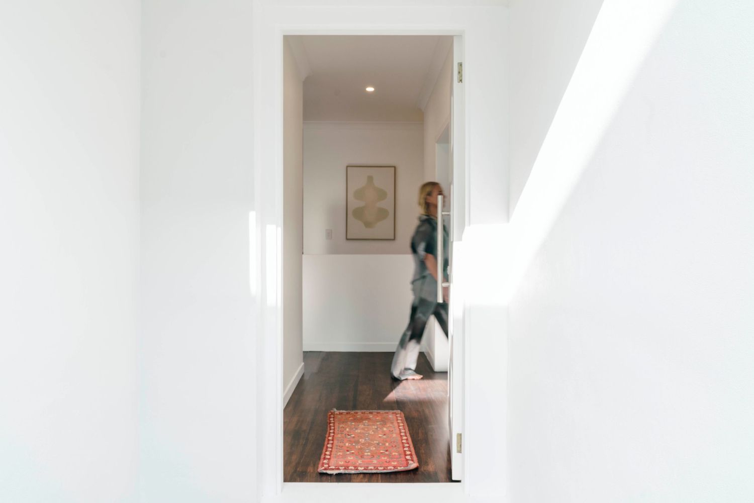 Minimalist white hallway with hardwood flooring and a decorative orange runner rug.