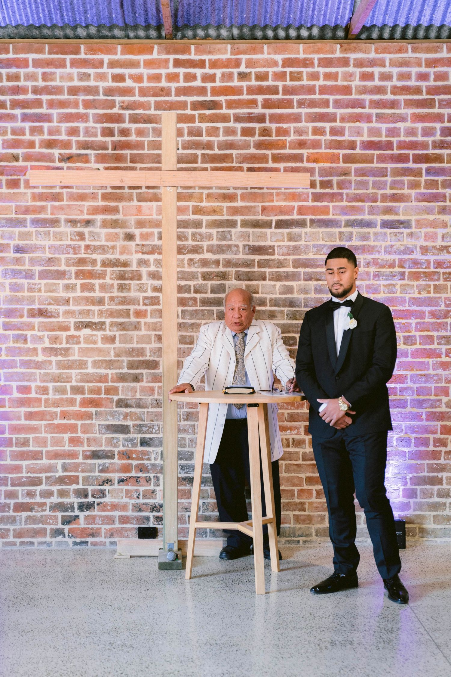 A wedding ceremony setup in front of a brick wall with a wooden cross and podium.