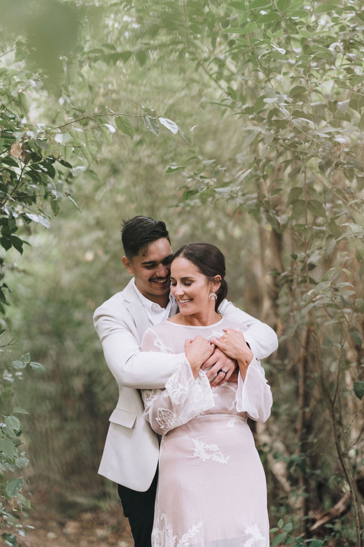 A couple embraces in a romantic moment among green foliage during their wedding photoshoot.