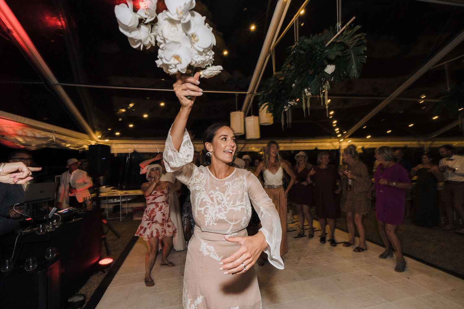 Wedding reception dance floor filled with celebratory guests under twinkling lights.