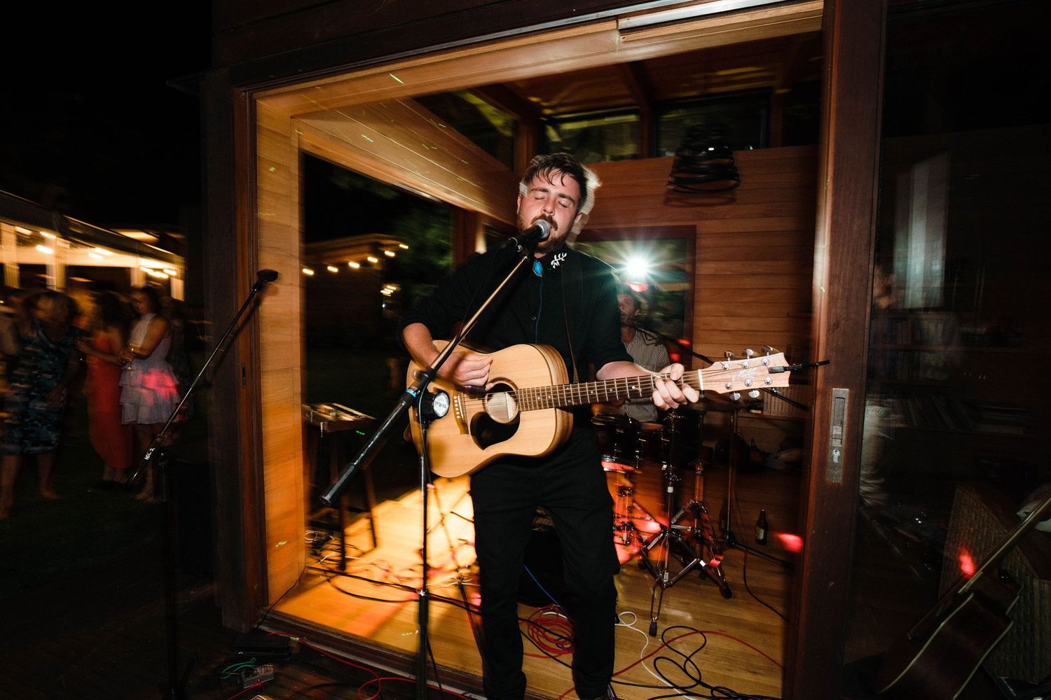 Musician performs with acoustic guitar in wooden-paneled venue space at night.
