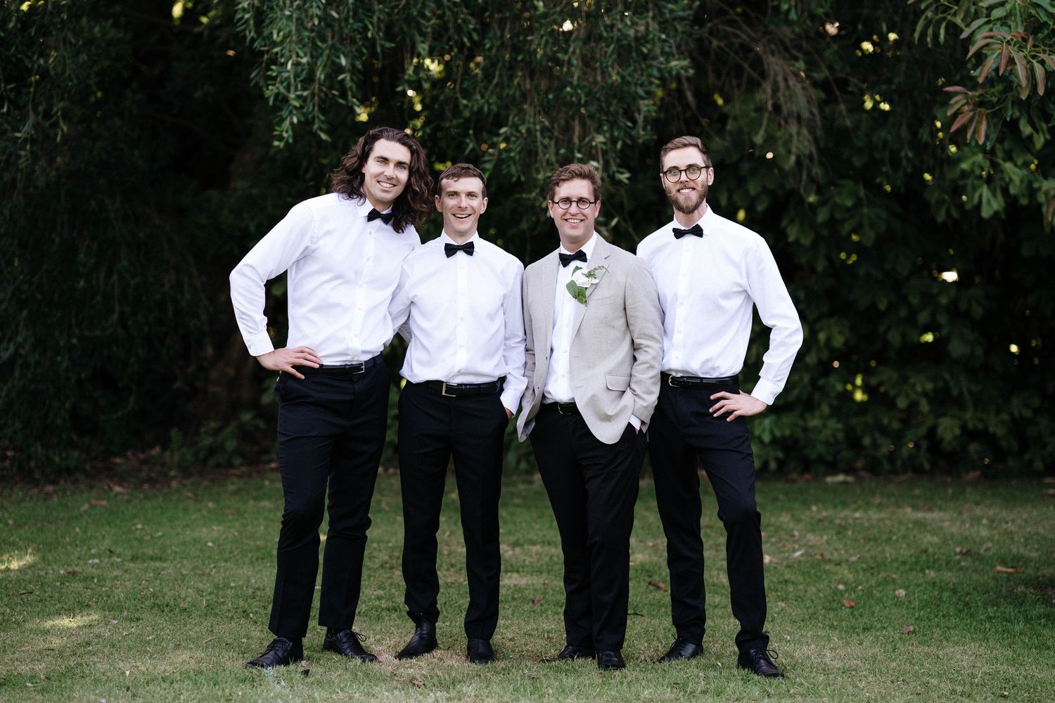 A formal group stands together on manicured lawn for wedding photos.