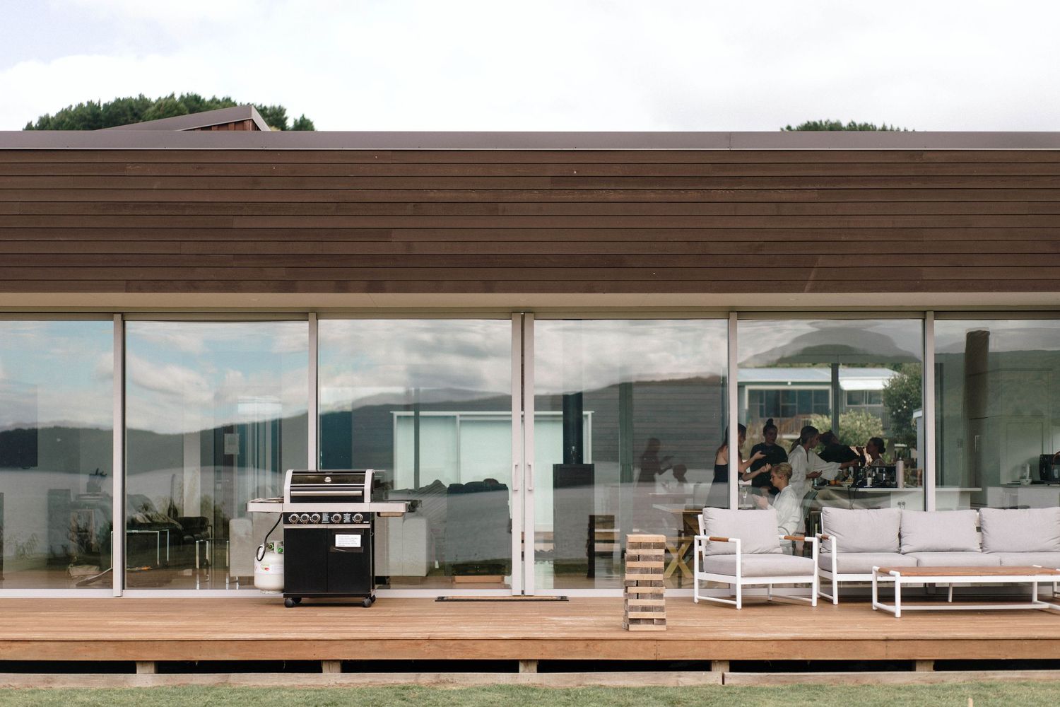 Modern glass-walled venue space with outdoor deck and barbecue grill overlooking scenic landscape.
