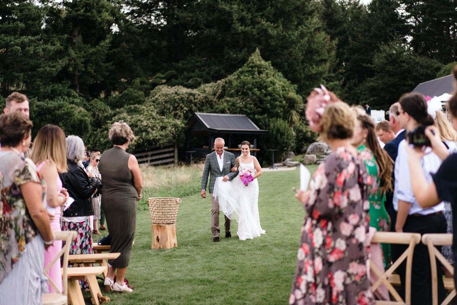 Wedding ceremony guests gathered on a grassy hillside watching the proceedings.