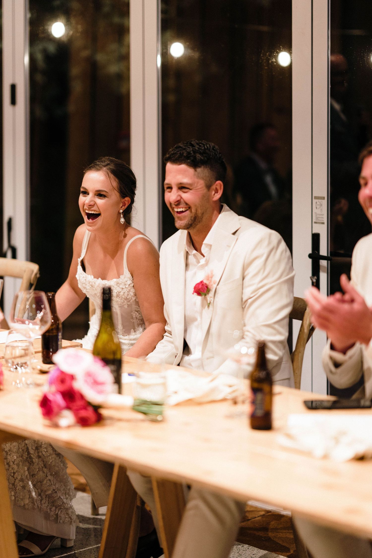 Wedding reception moment at a table with floral decor and wine bottles.