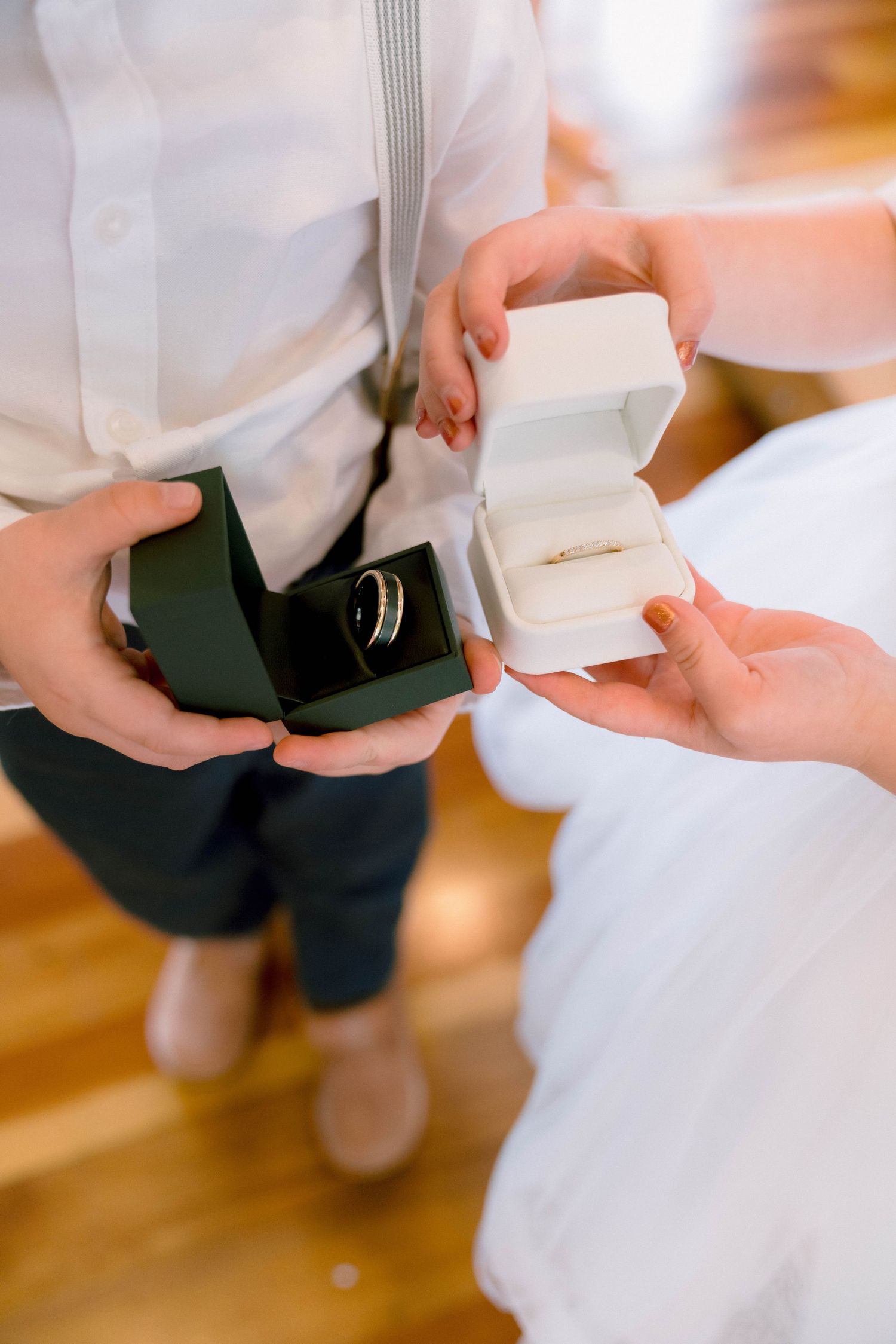Ring bearer presents wedding rings in small green and white boxes during wedding ceremony.