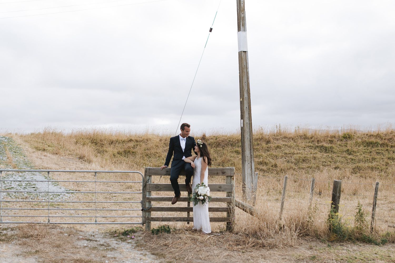 A romantic couple sits on a rustic wooden bench in a serene countryside setting during golden hour.